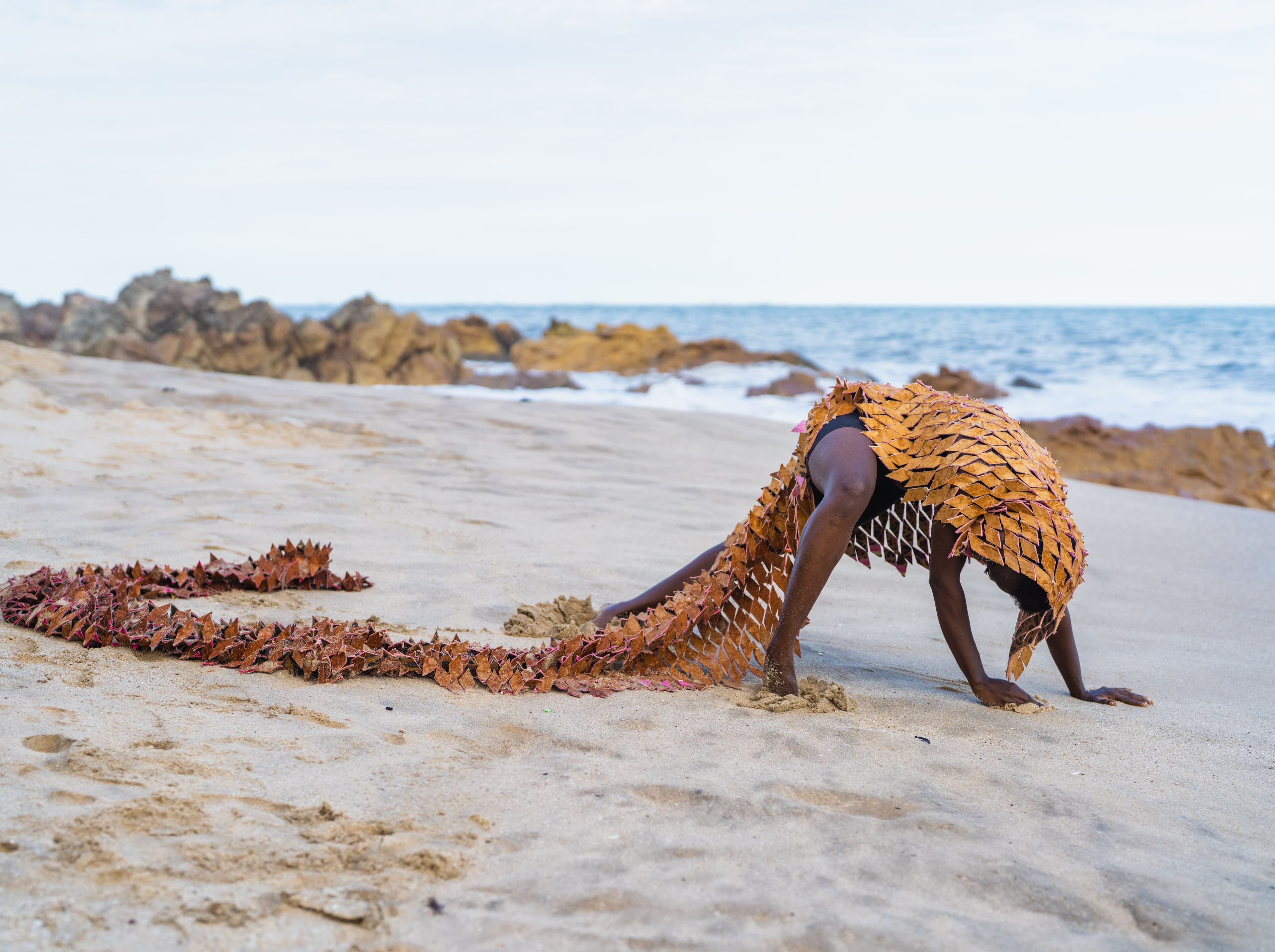 Person wearing a leaf-like costume on a sandy beach by the sea