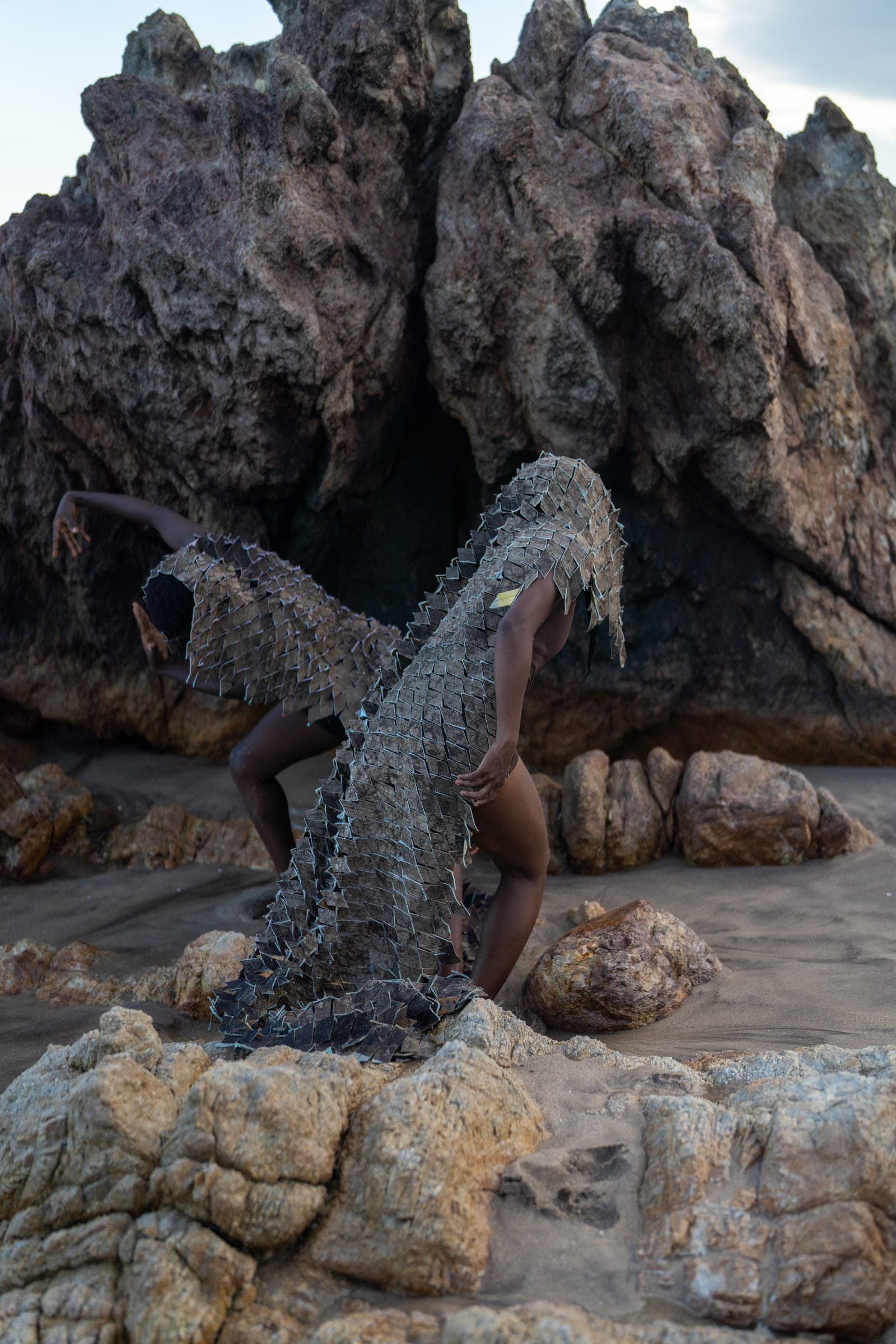 Performer in a textile garment among coastal rocks
